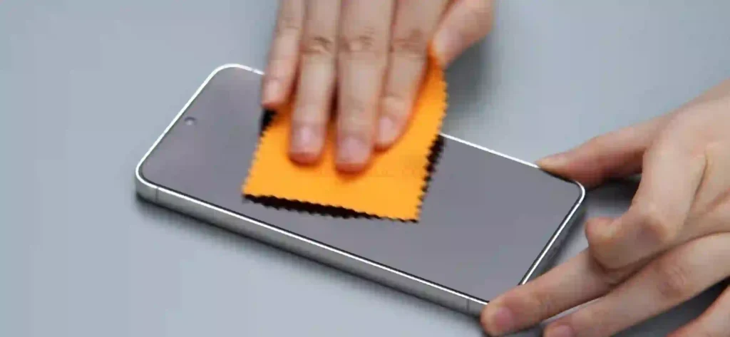 Cleaning Samsung Galaxy A56 display with an orange microfiber cloth to remove dust before screen protector installation